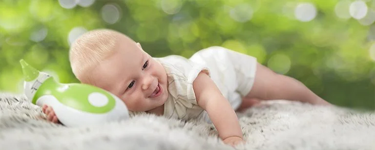 Little boy lying on his belly, holding a Nosiboo Go portable electric nasal aspirator