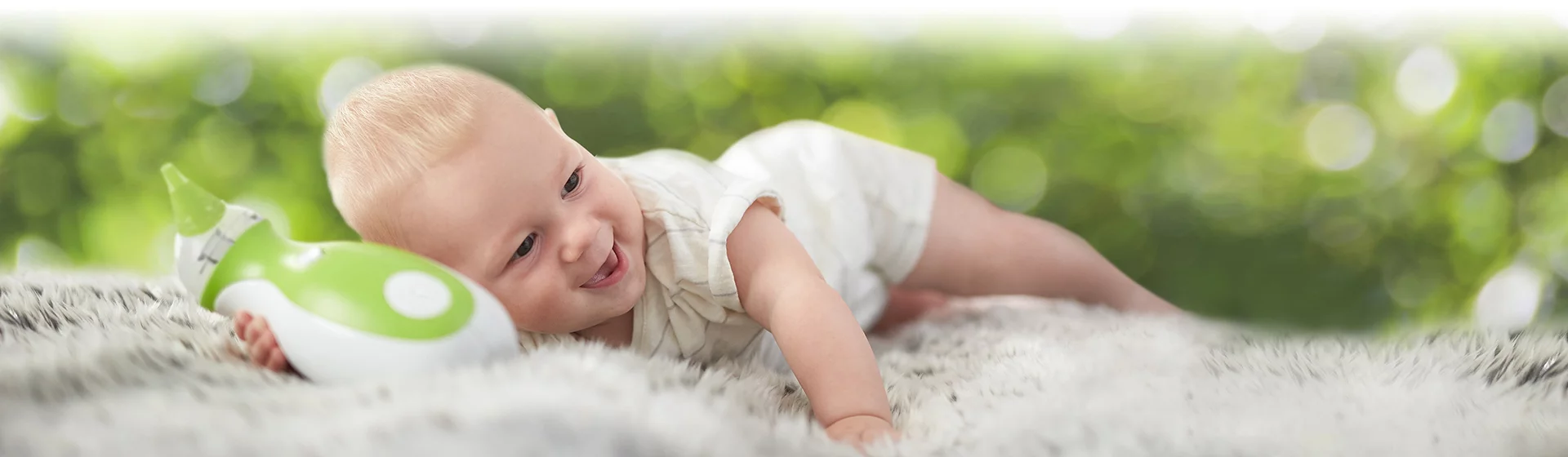 Little boy lying on his belly, holding a Nosiboo Go portable electric nasal aspirator