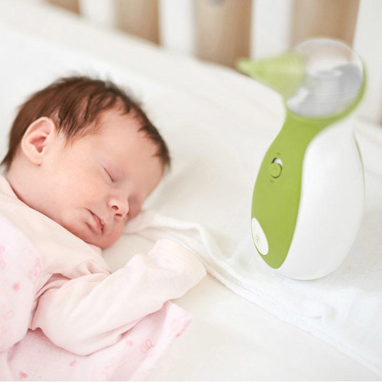 A baby boy sleeping peacefully in his bed next to the Nosiboo Go Portable Nasal Aspirator