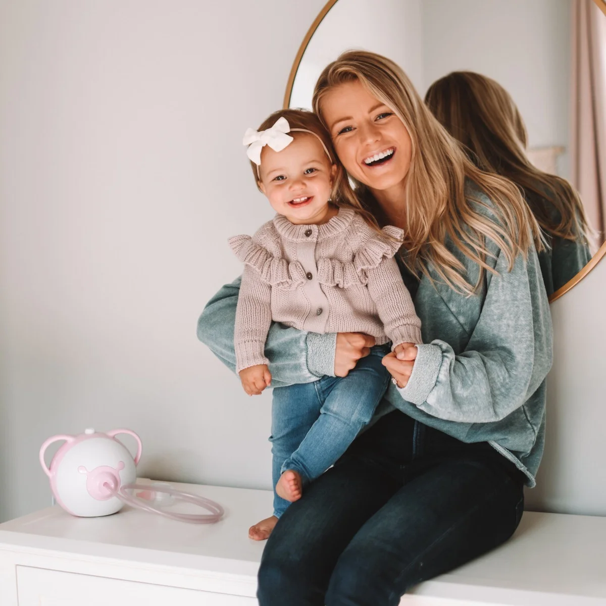 Smiling mom with her daughter, next to them a pink Nosiboo Pro electric nasal aspirator on the shelf