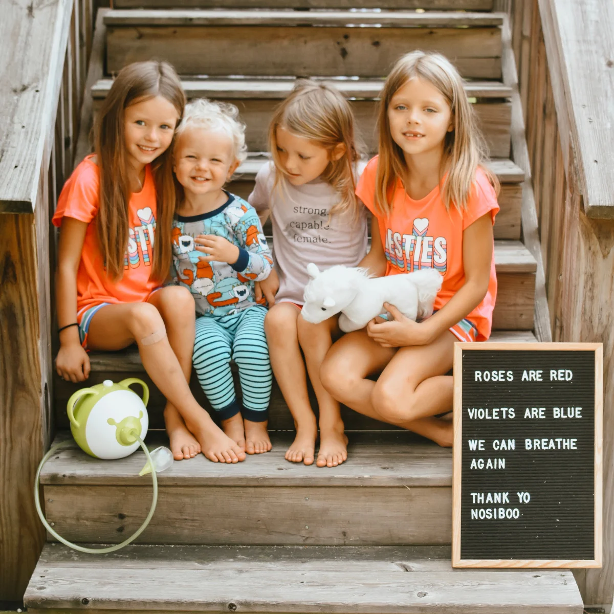 4 happy siblings sitting on the stairs next to a Nosiboo Pro electric nasal aspirator