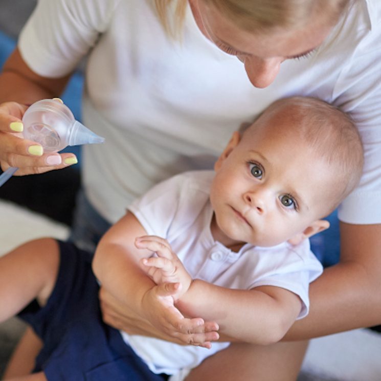 A cute, little boy held by his mother who is going to clear his nose with the help of the Nosiboo Pro Electric Nasal Aspirator