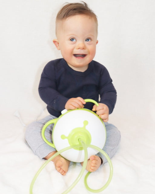 Little boy with Down syndrome sitting on a bed, holding a Nosiboo Pro electric nasal aspirator