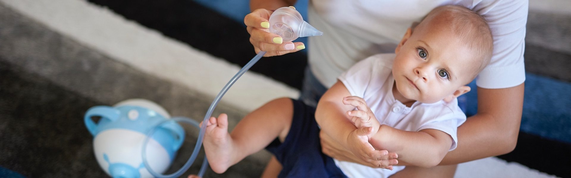 A cute, little boy held by his mother who is going to clear his nose with the help of the Nosiboo Pro Electric Nasal Aspirator