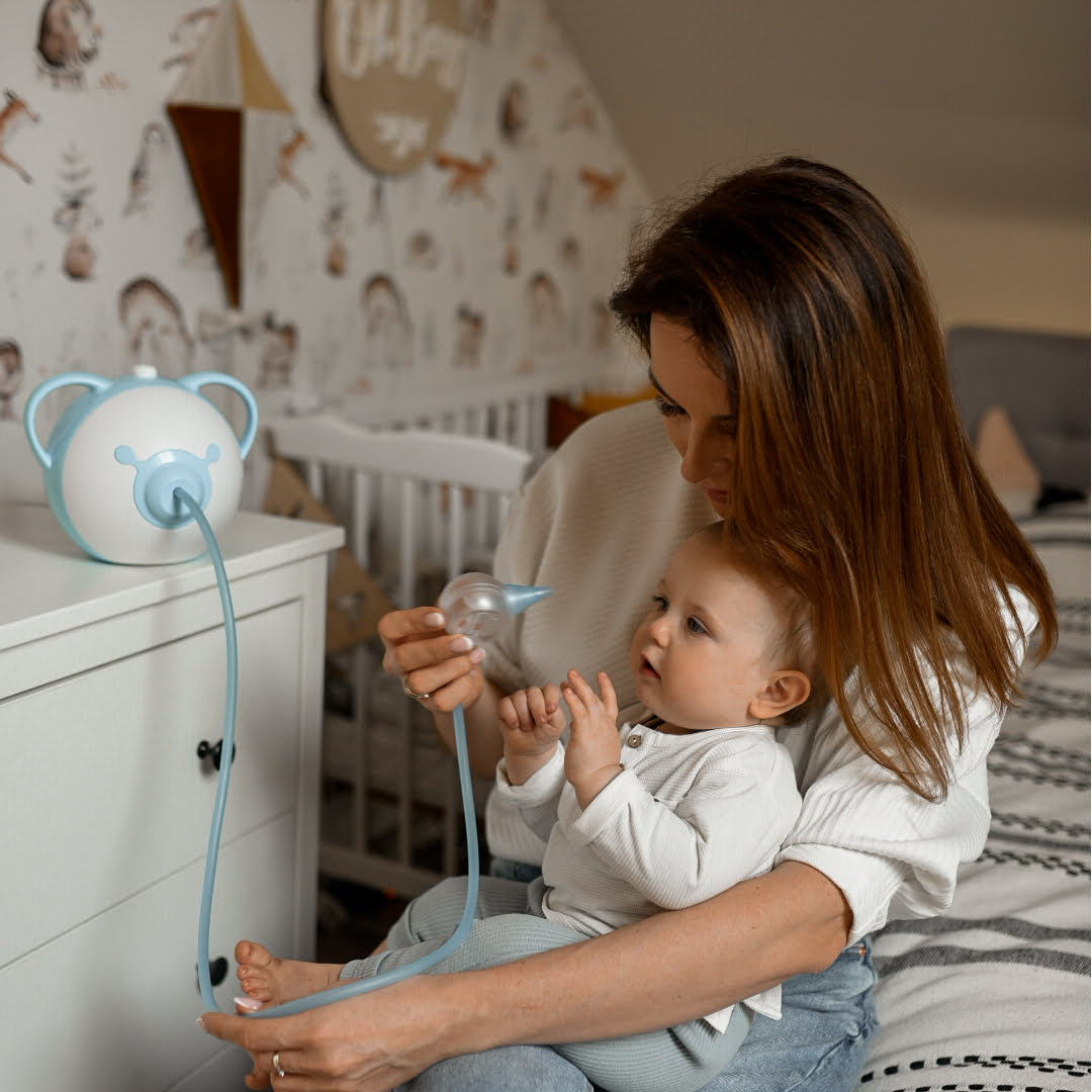 A mother with her son sitting on a couch, holding a Nosiboo Pro electric nasal aspirator