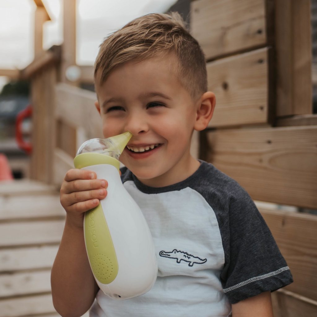 Smiling little boy holding a Nosiboo Go portable electric nasal aspirator