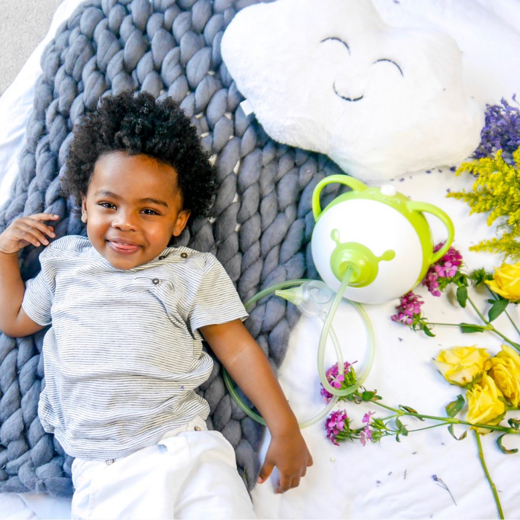 Smiling little boy holding a Nosiboo Go portable electric nasal aspirator