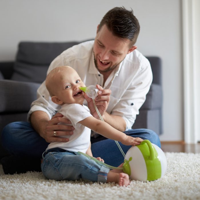 A dad clearing his son's nose with the help of a baby nasal aspirator Nosiboo Pro