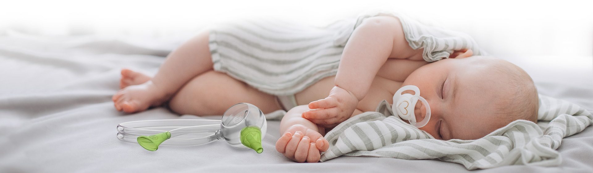 A baby boy sleeping peacefully in a bed next to the Nosiboo Eco Manual Nasal Aspirator